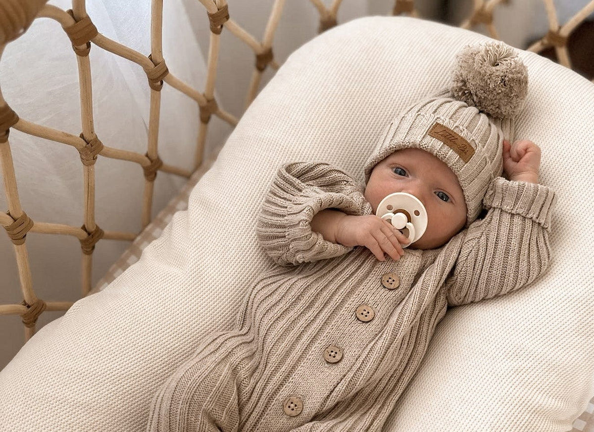 A newborn romper in beige color with vintage wooden buttons, lying on a white textile surface.