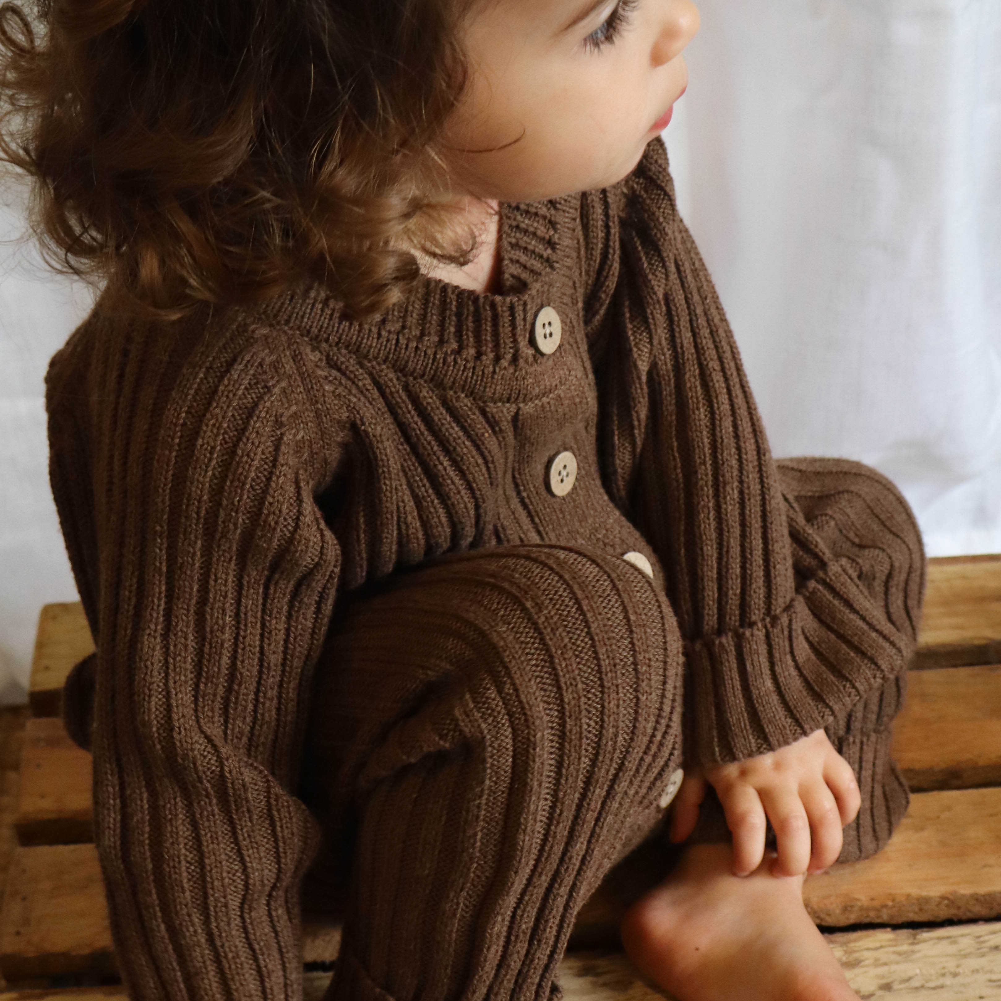 young girl sitting on timber crate wearing chocolate brown knitted romper with buttons