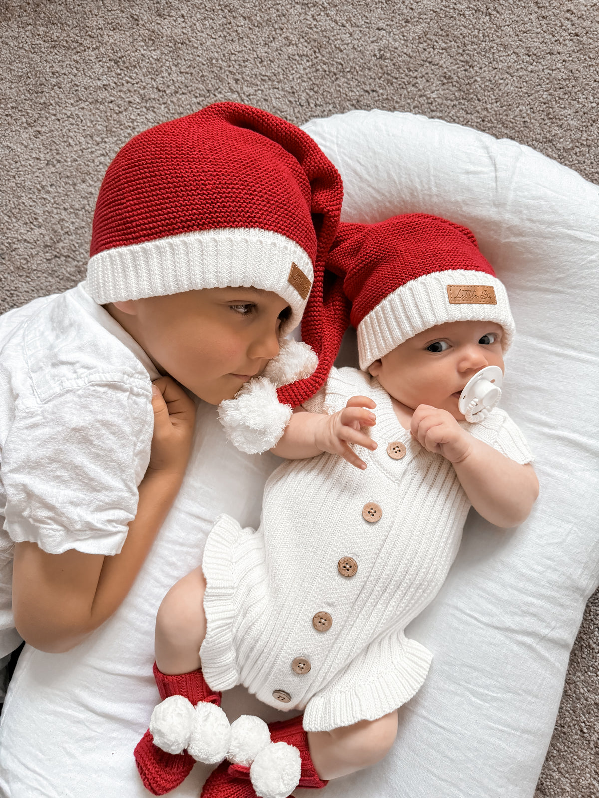 Two children wearing Little B's Knitted Cotton Classic Christmas Beanies in red