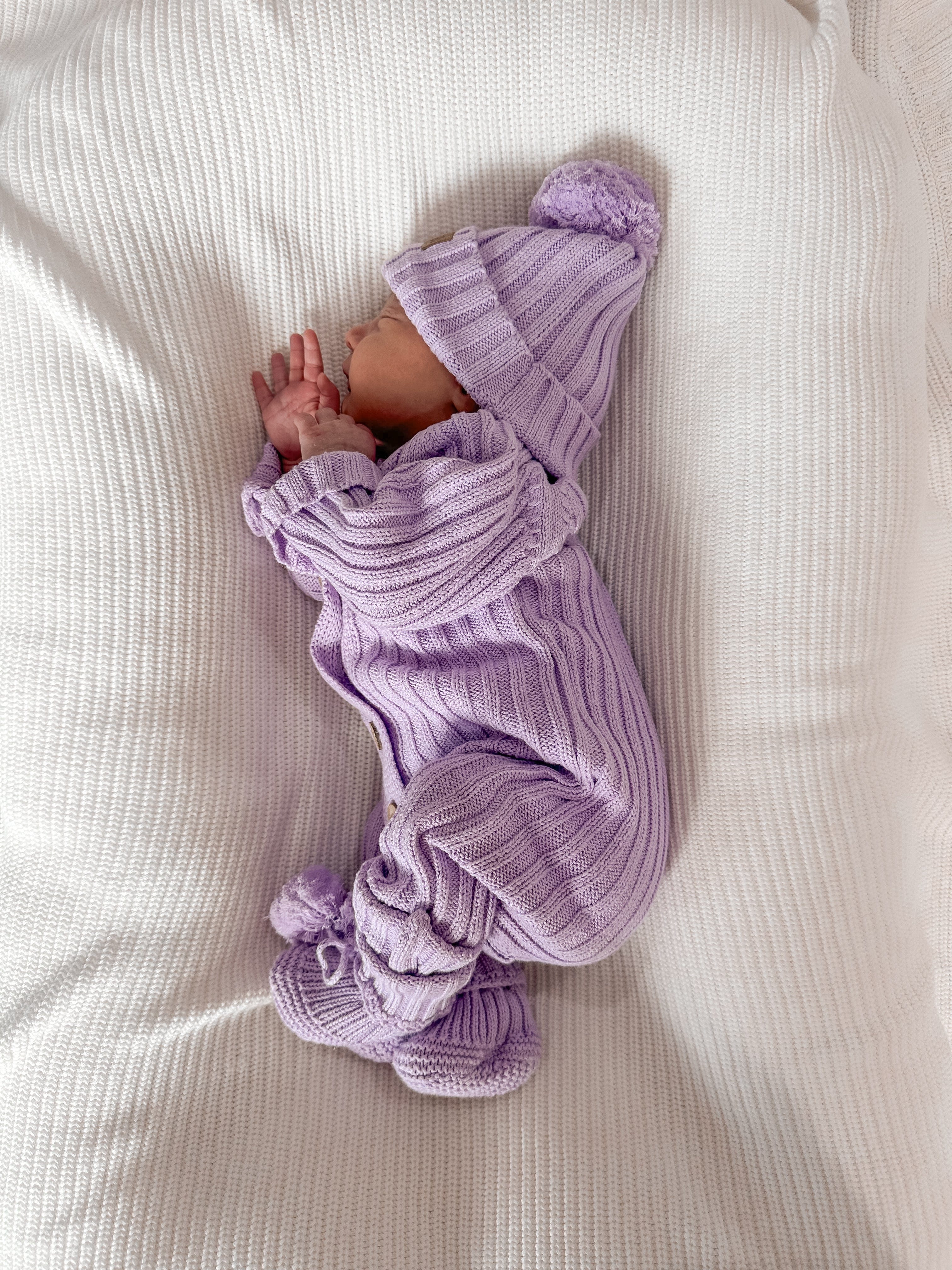 Newborn baby sleeping on a white blanket, wearing a purple Knitted Cotton Ribbed Beanie from Little B's Retail