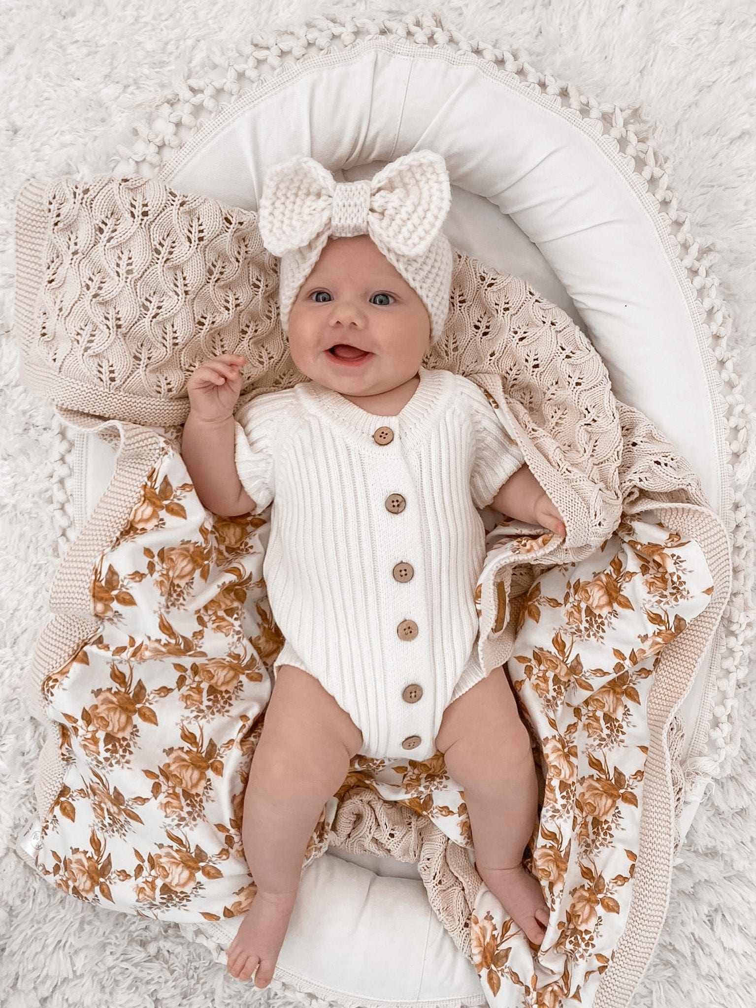 Baby in Little B's Knitted Cotton Short Ribbed Romper - Milk, with a bow headband and floral blanket