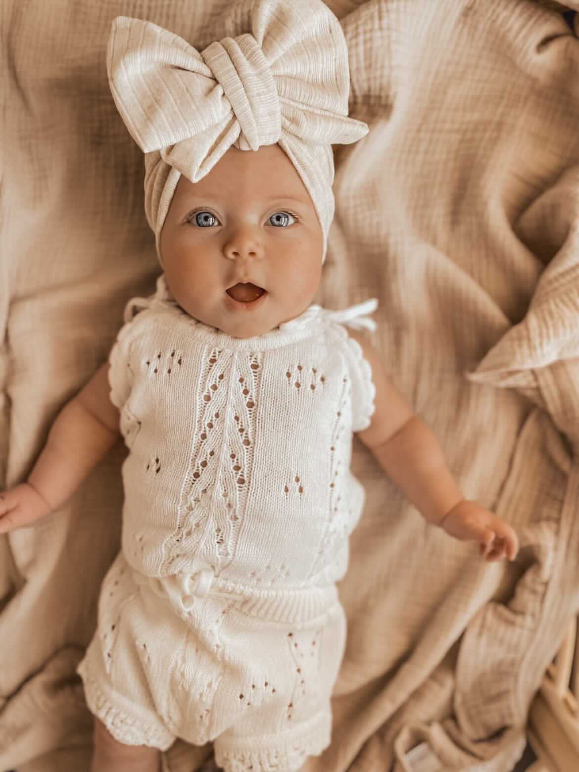 Little B's Knitted Cotton Pointelle Set in Milk on a baby with a matching bow headband