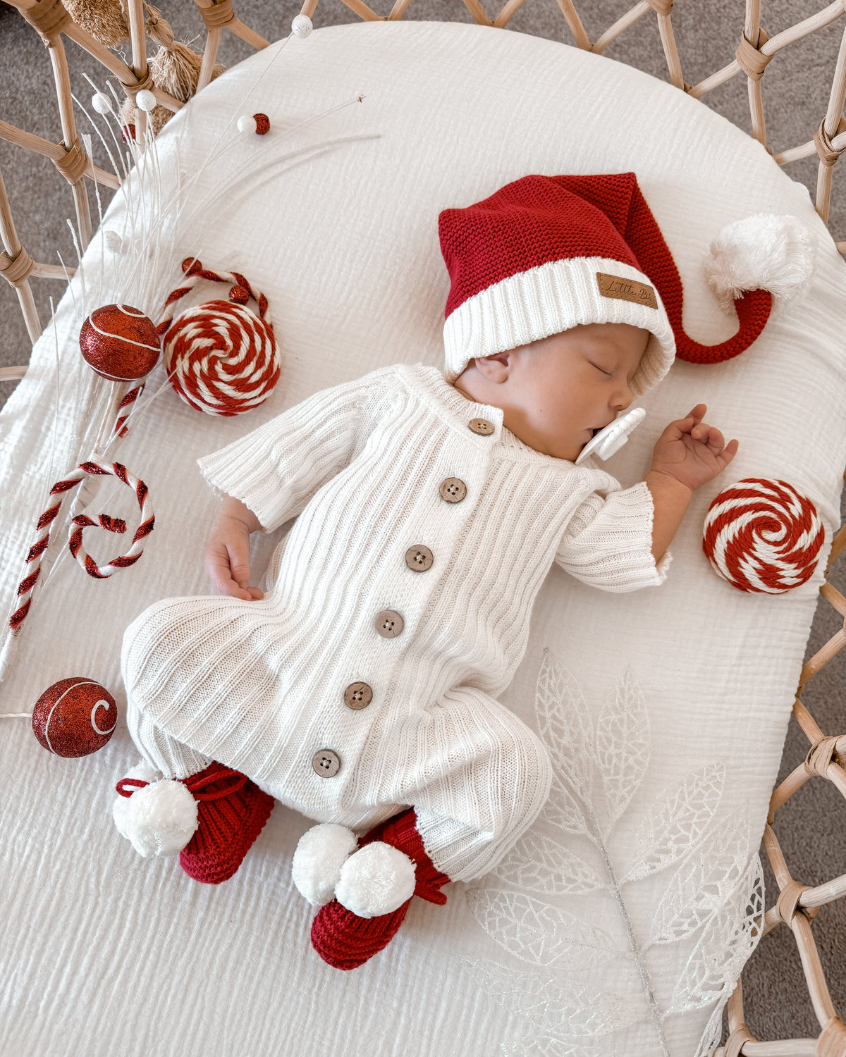 Sleeping baby in a white knitted outfit, red Santa hat, and Little B's Knitted Pom Pom Booties