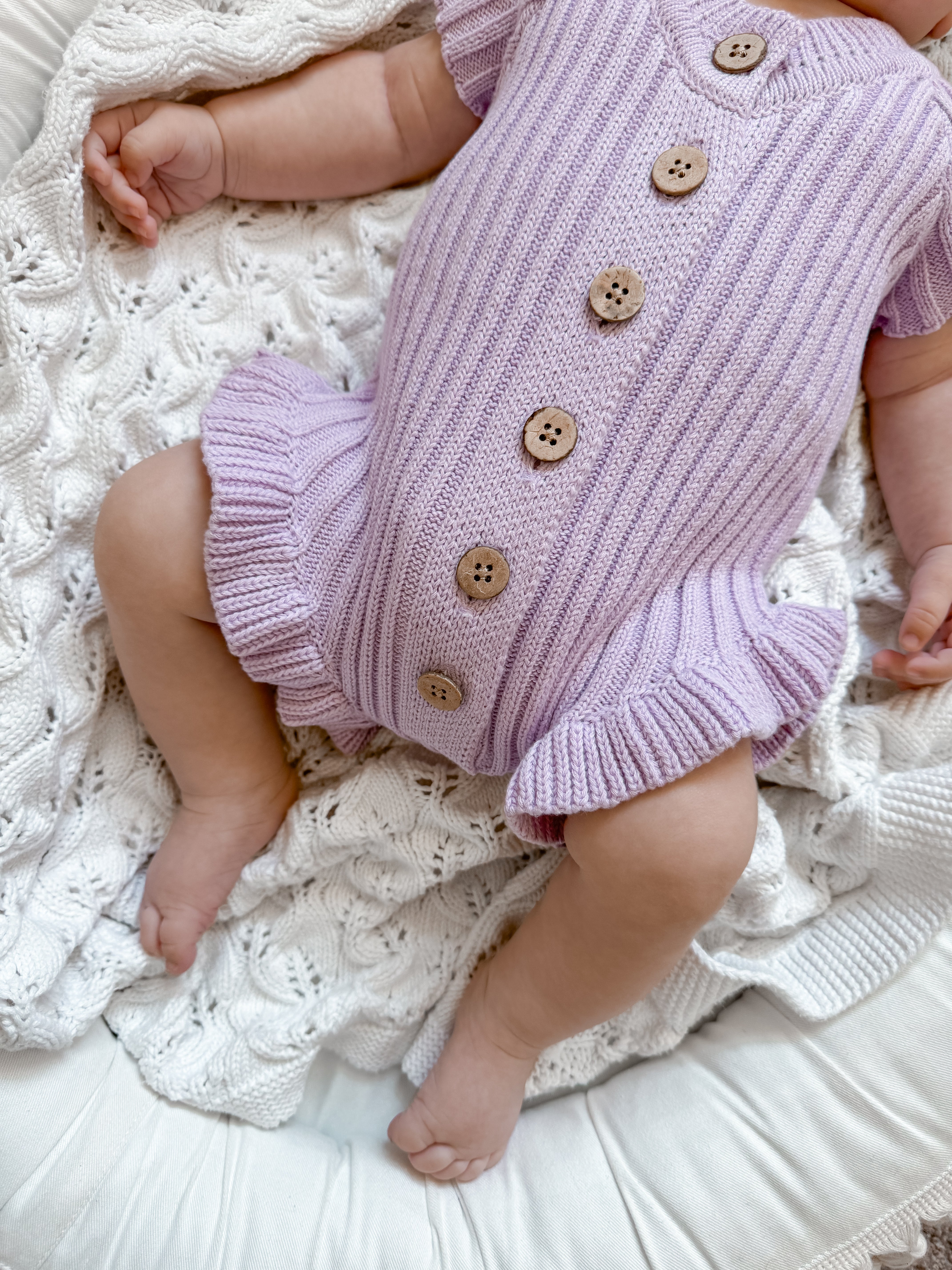 Little B's Knitted Cotton Ribbed Ruffle Romper in purple with wooden buttons on a baby