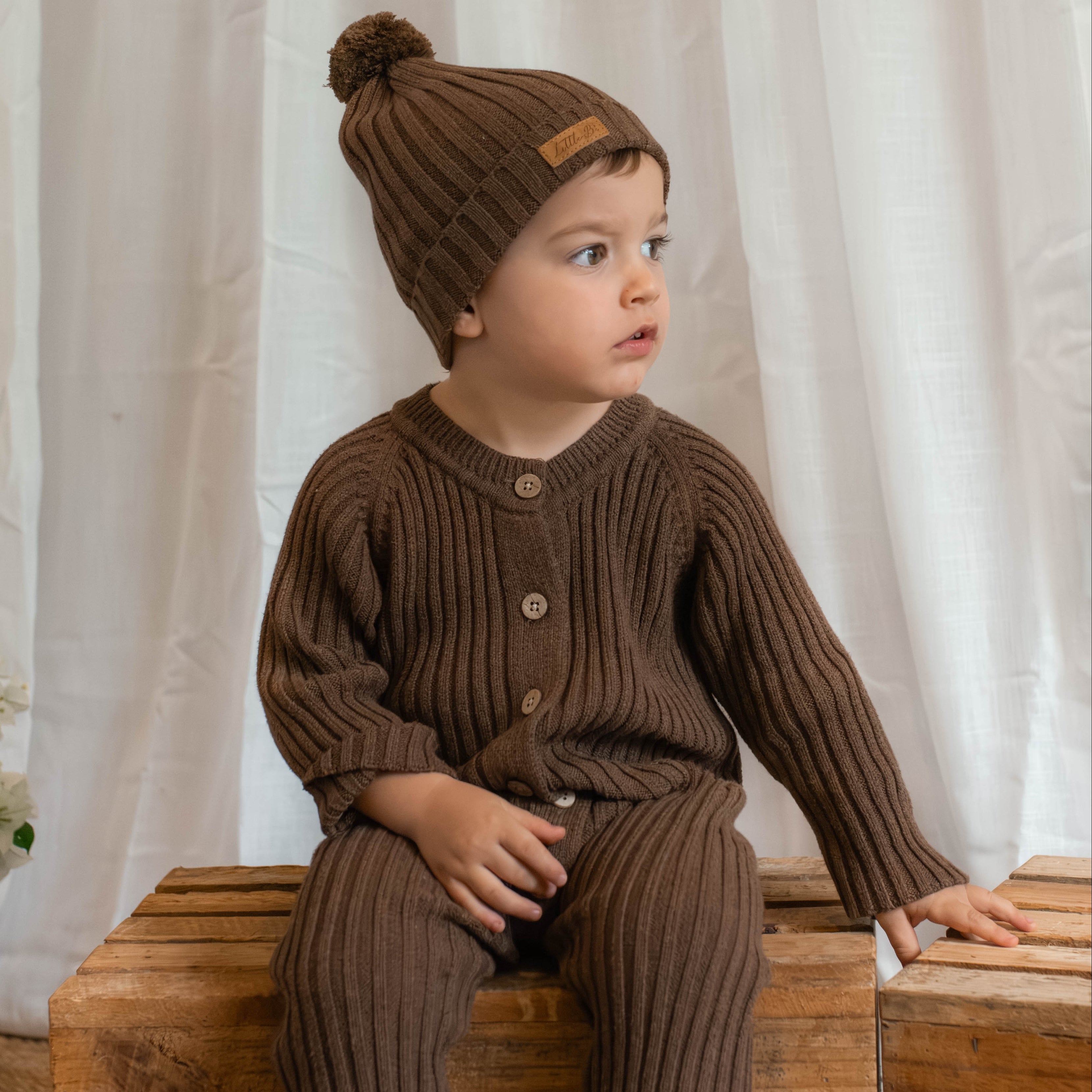 Boy sitting on timber crate wearing knitted cotton brown ribbed romper and matching beanie