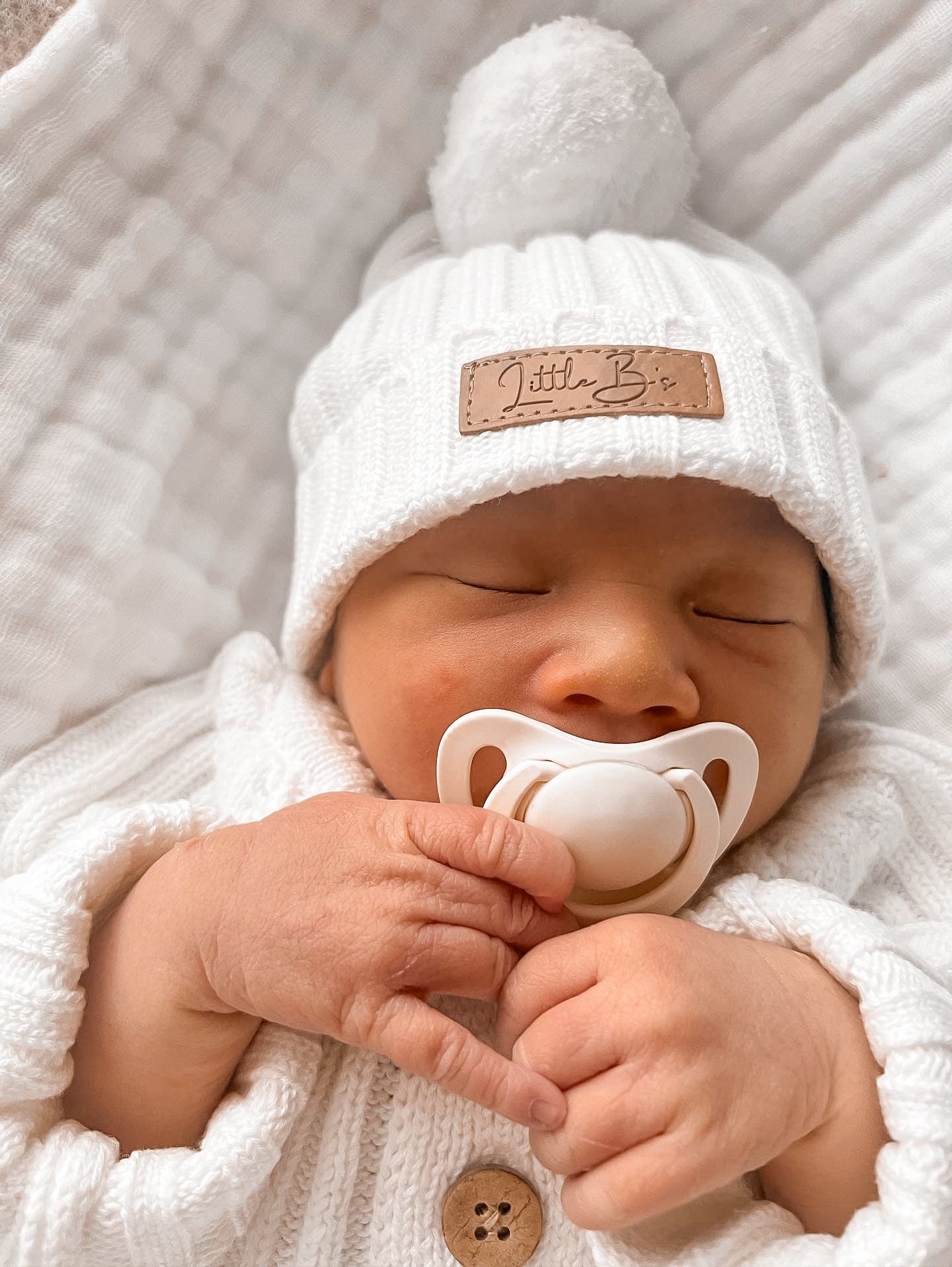 Sleeping baby wearing a Little B's Knitted Cotton Ribbed Beanie in Milk and holding a pacifier