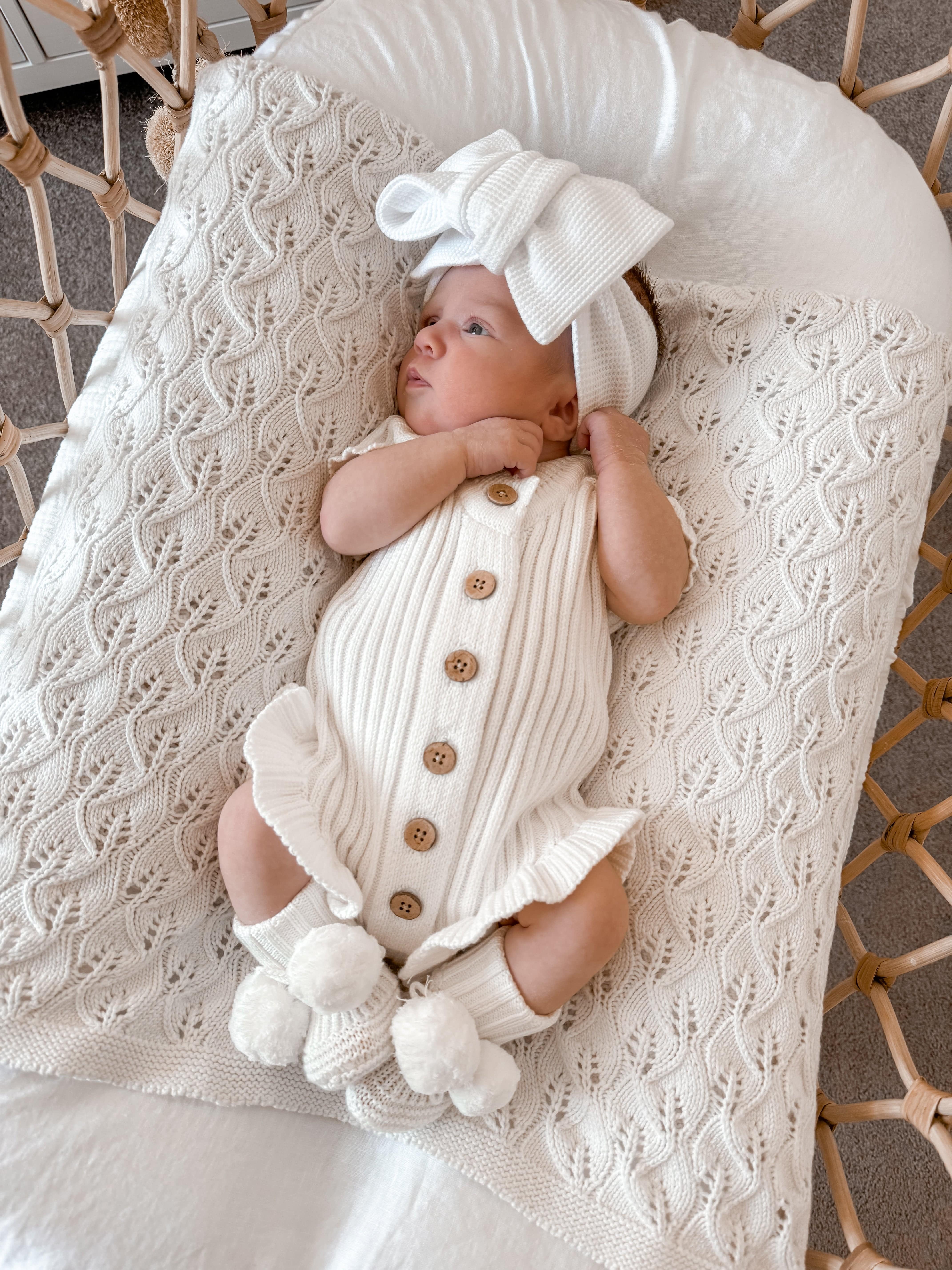 Newborn baby in a Little B's Knitted Cotton Ribbed Ruffle Romper - Milk, with a matching bow