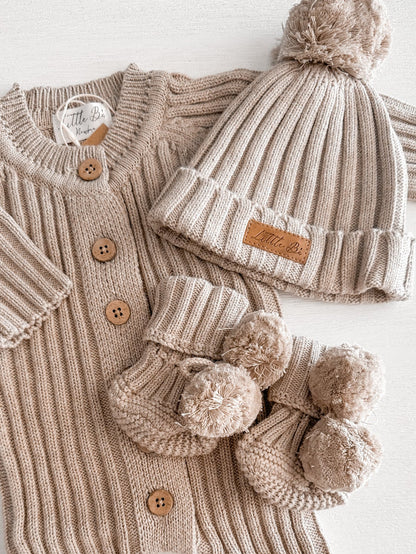 Ribbed neutral brown coloured cotton booties with pom poms and matching beanie on top of a matching romper
