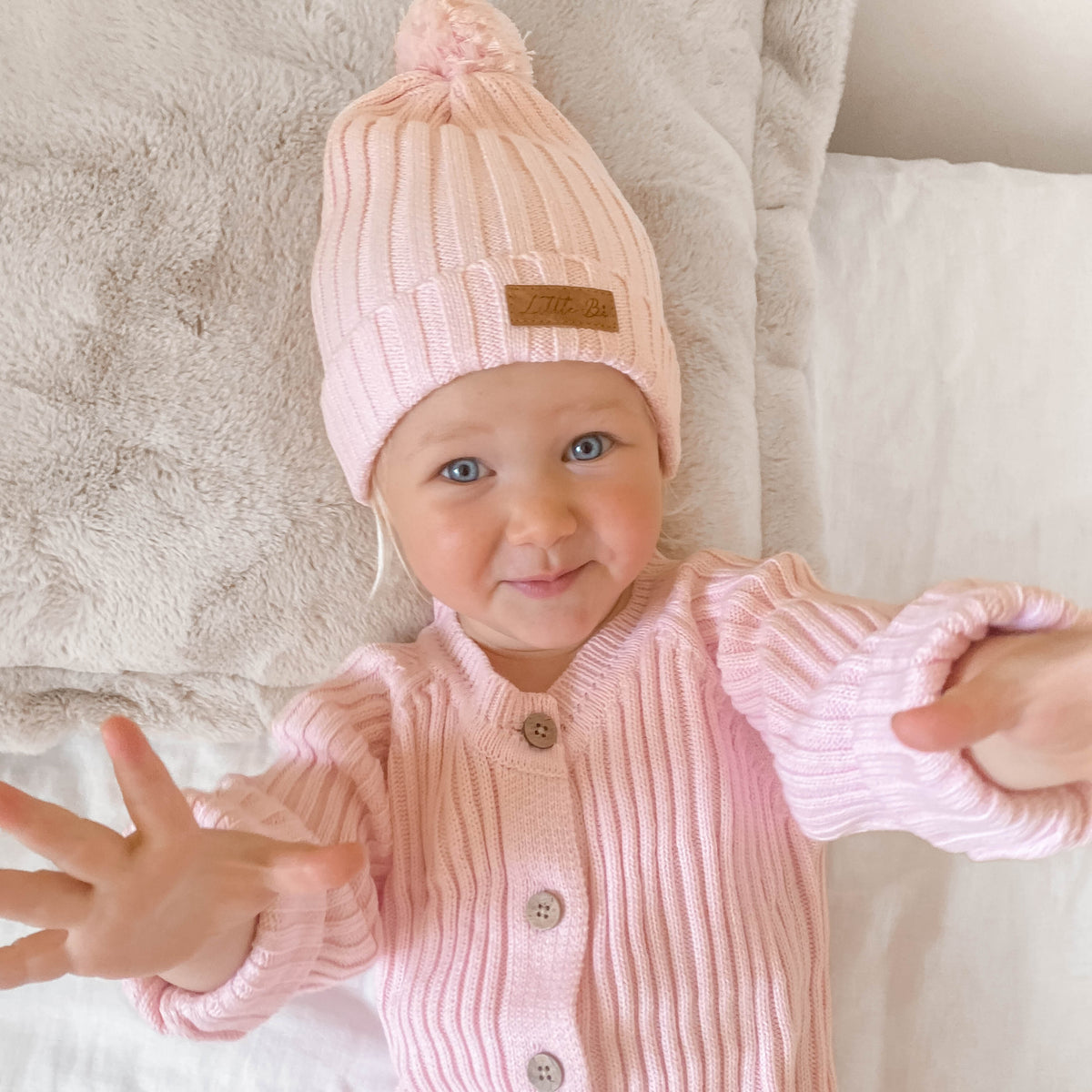 Baby wearing a pink knit outfit with a matching hat on a soft surface