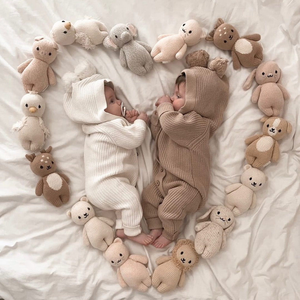 Two babies in knitted rompers surrounded by a heart shape of knitted animal toys